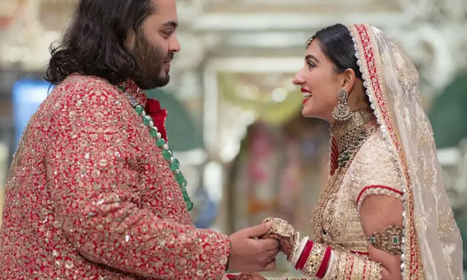 Anant Ambani matrimonio: la sposa sorride guardando lo sposo, entrambi vestiti con abiti tradizionali riccamente decorati.