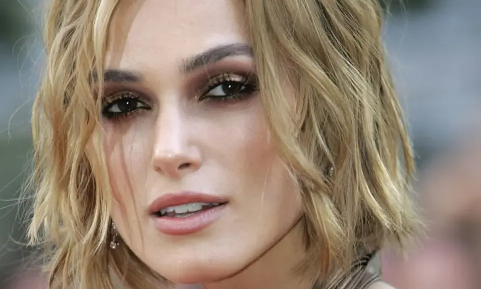 Primo piano di una donna con taglio butterfly capelli corti biondi, trucco occhi intenso e labbra rosa.