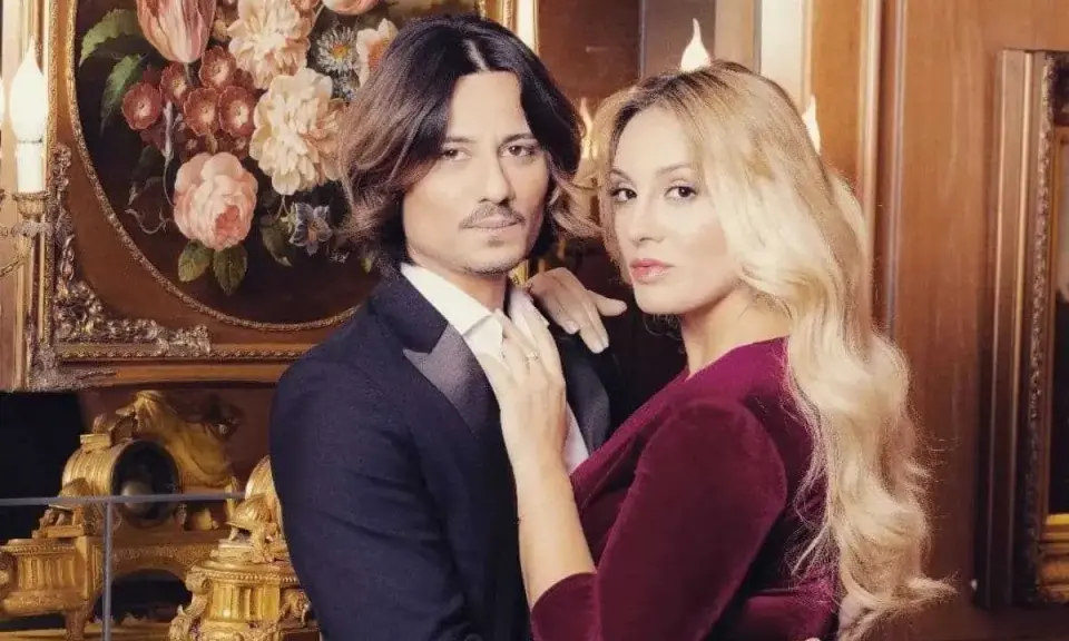 Francesca Manzini e il suo fidanzato, un abbraccio elegante davanti a un quadro di fiori e un orologio dorato.