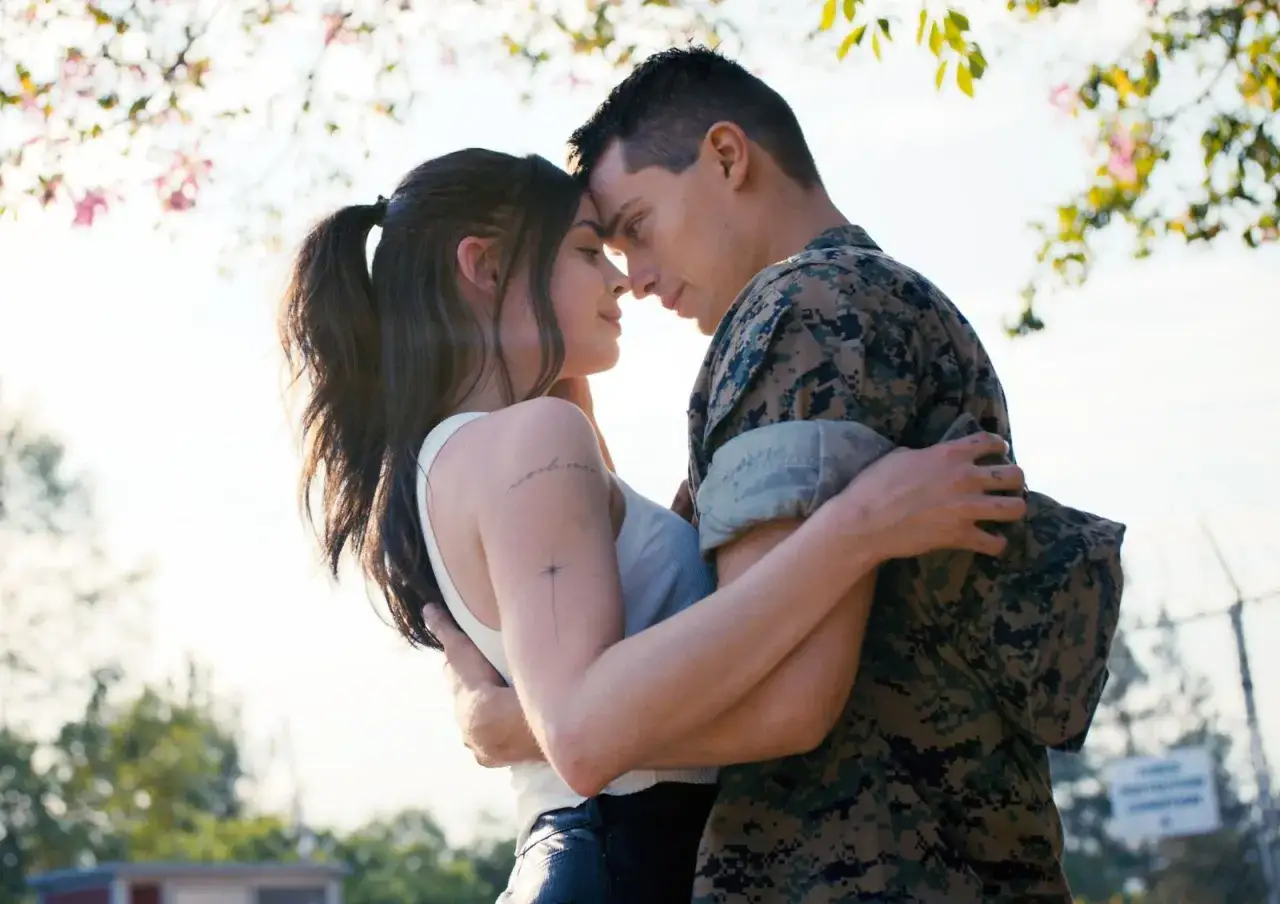 Nicholas Galitzine, in uniforme militare, abbraccia teneramente la sua fidanzata sotto un albero fiorito.