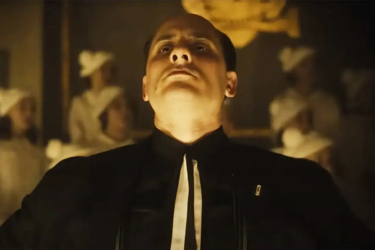 Un uomo con un'espressione intensa, vestito di nero, sullo sfondo figure sfocate. La serie tv