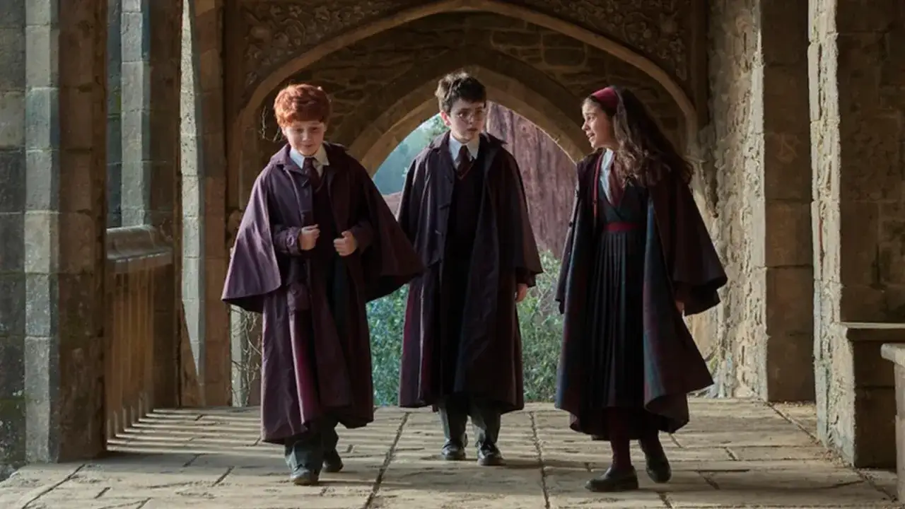 Tre giovani maghi, con mantelli scuri, camminano in un corridoio di Hogwarts, anticipando la nuova harry potter serie tv.
