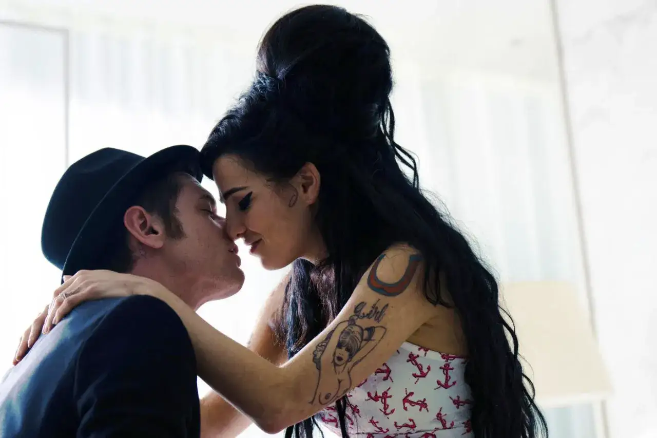 Blake Fielder-Civil, marito di Amy Winehouse, la bacia teneramente. Lei ha tatuaggi visibili sul braccio.