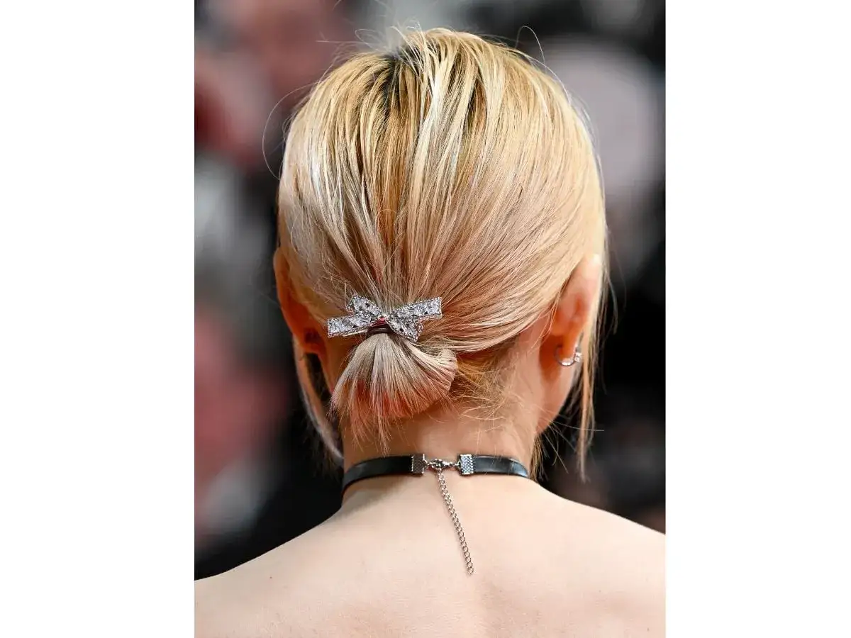 Acconciature capelli corti: un elegante chignon basso con fermaglio a fiocco scintillante, che completa un look raffinato.