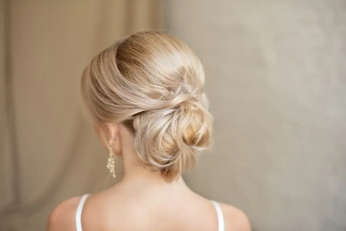 Chignon basso cerimonia elegante, con capelli biondi raccolti morbidamente.