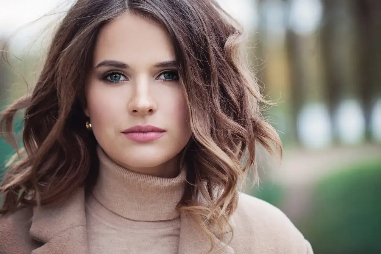 Primo piano di una donna con capelli sottili e pochi, castani e mossi, che incorniciano il viso. Indossa un maglione a collo alto color cammello.