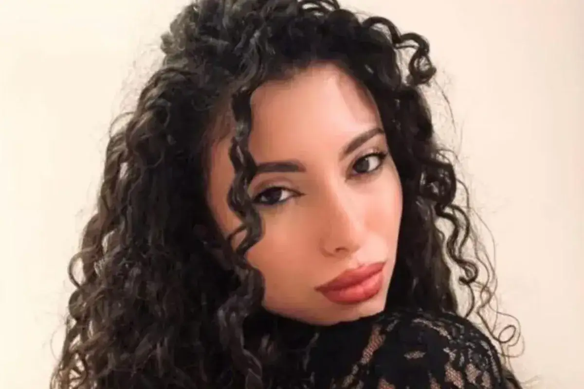La nuova fidanzata di Raimondo Todaro, con lunghi capelli ricci e un abito di pizzo nero, sorride con labbra rosse.