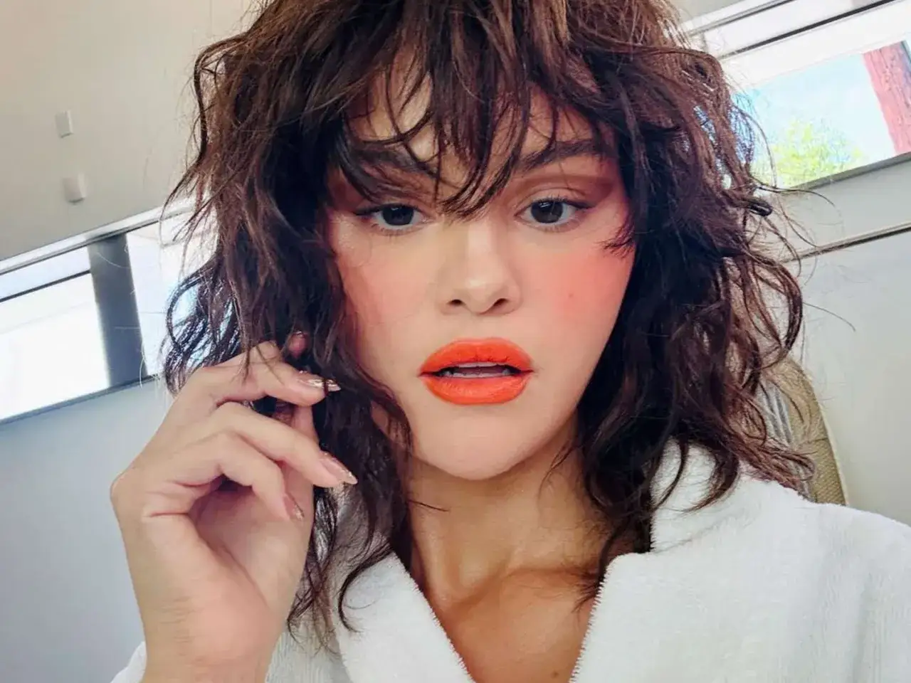 Selena Gomez con un audace taglio wolf cut, labbra arancioni e blush acceso.