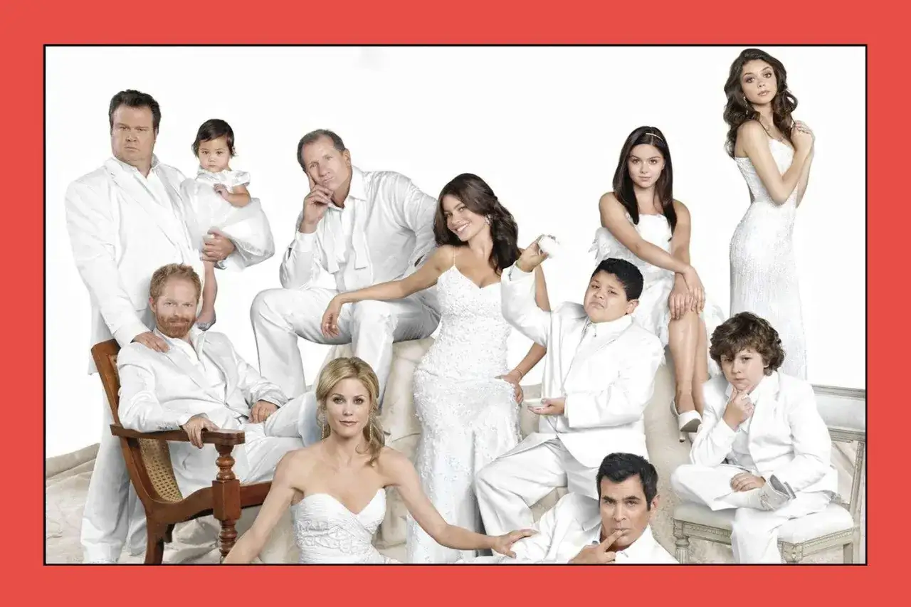 Il cast di Modern Family posa in abiti bianchi. Una famiglia allargata, con bambini e adulti, tutti sorridenti.