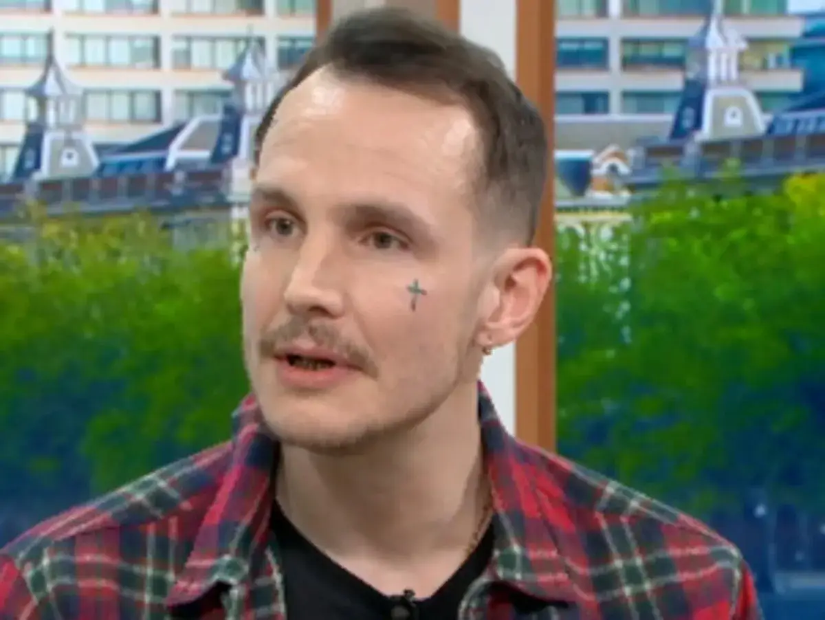 Blake Fielder-Civil oggi, con un tatuaggio a forma di croce sul viso, parla in televisione.