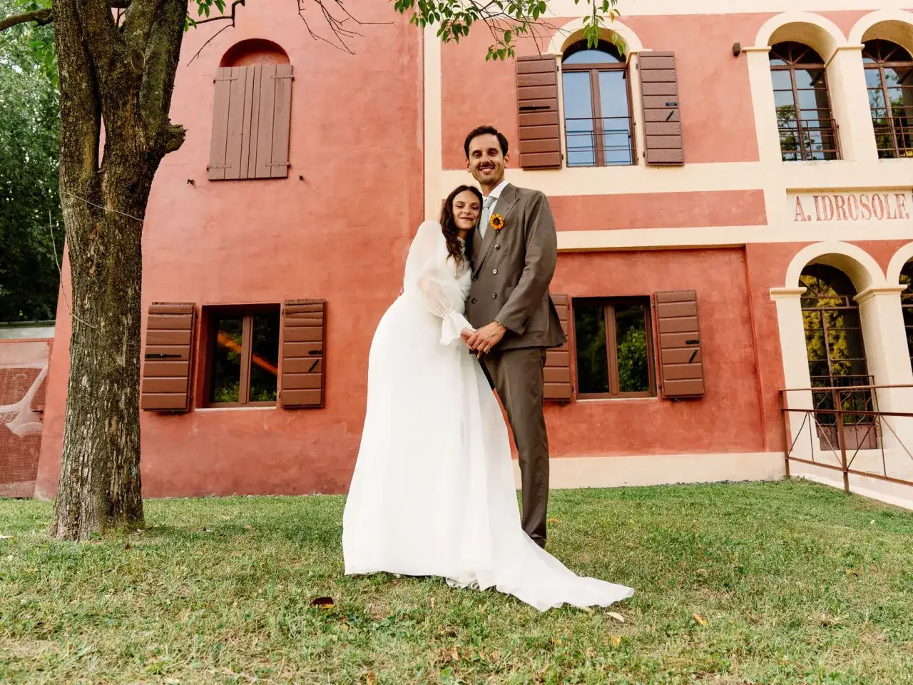 Francesca Michielin e il suo sposo felici davanti a un edificio rosso, un'immagine che evoca il loro matrimonio.
