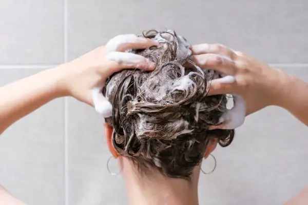 Mani che massaggiano shampoo sui capelli bagnati, schiuma abbondante. La domanda "ogni quanto lavare i capelli" è centrale per una chioma sana.