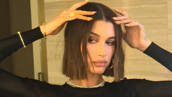 Modello con capelli castani, lisci e pochi, che sfoggia un taglio a caschetto. Indossa gioielli d'oro e un abito nero.