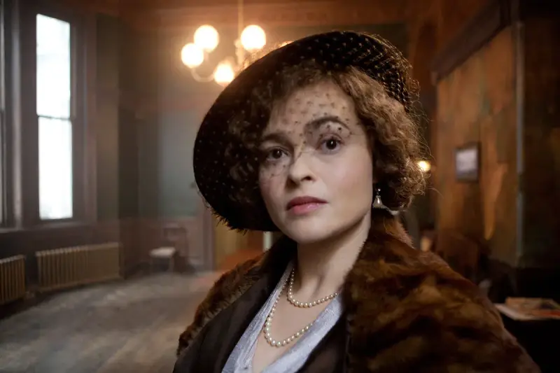 Helena Bonham Carter, con cappello e velo, indossa una pelliccia e perle. Scena da un film.